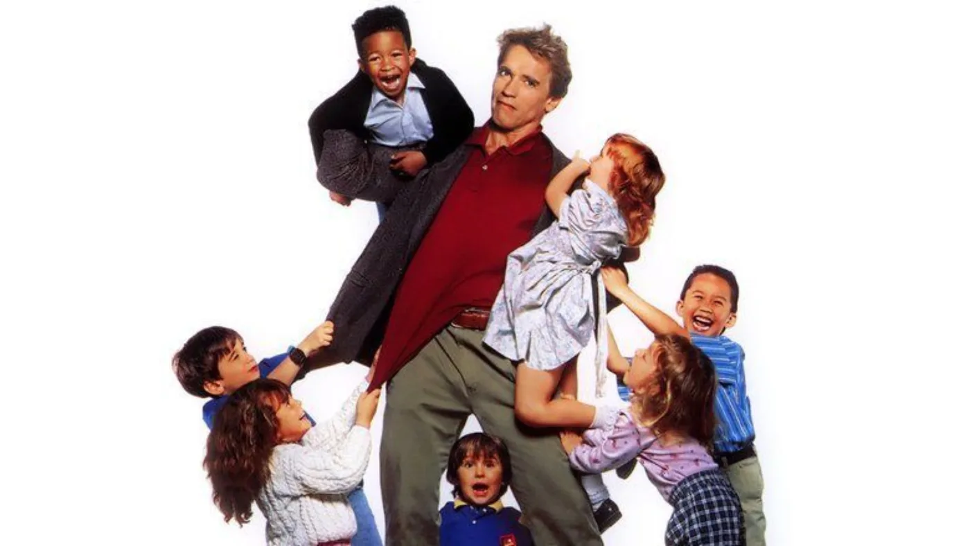 Das Bild zeigt Arnold Schwarzenegger als Polizist, der in einem Kindergarten arbeitet.